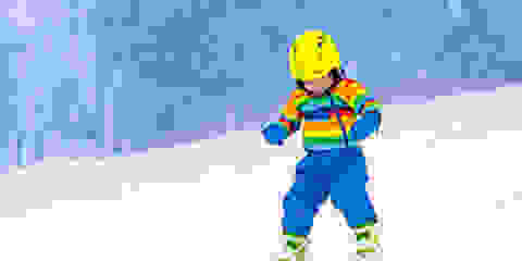 Ein kleines Kinder fährt in Skischuhen und Skiern eine Piste hinab.