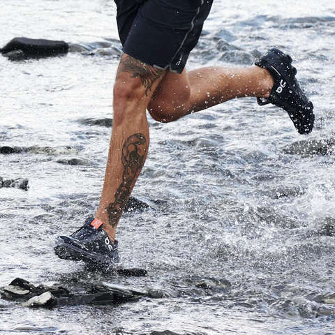 Ein Läufer läuft mit wasserdichten Laufschuhen von On durch einen Fluss.