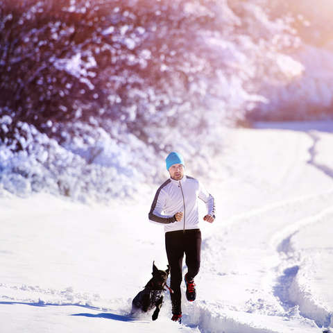 Ein Mann joggt mit Hund durch eine Winterlandschaft