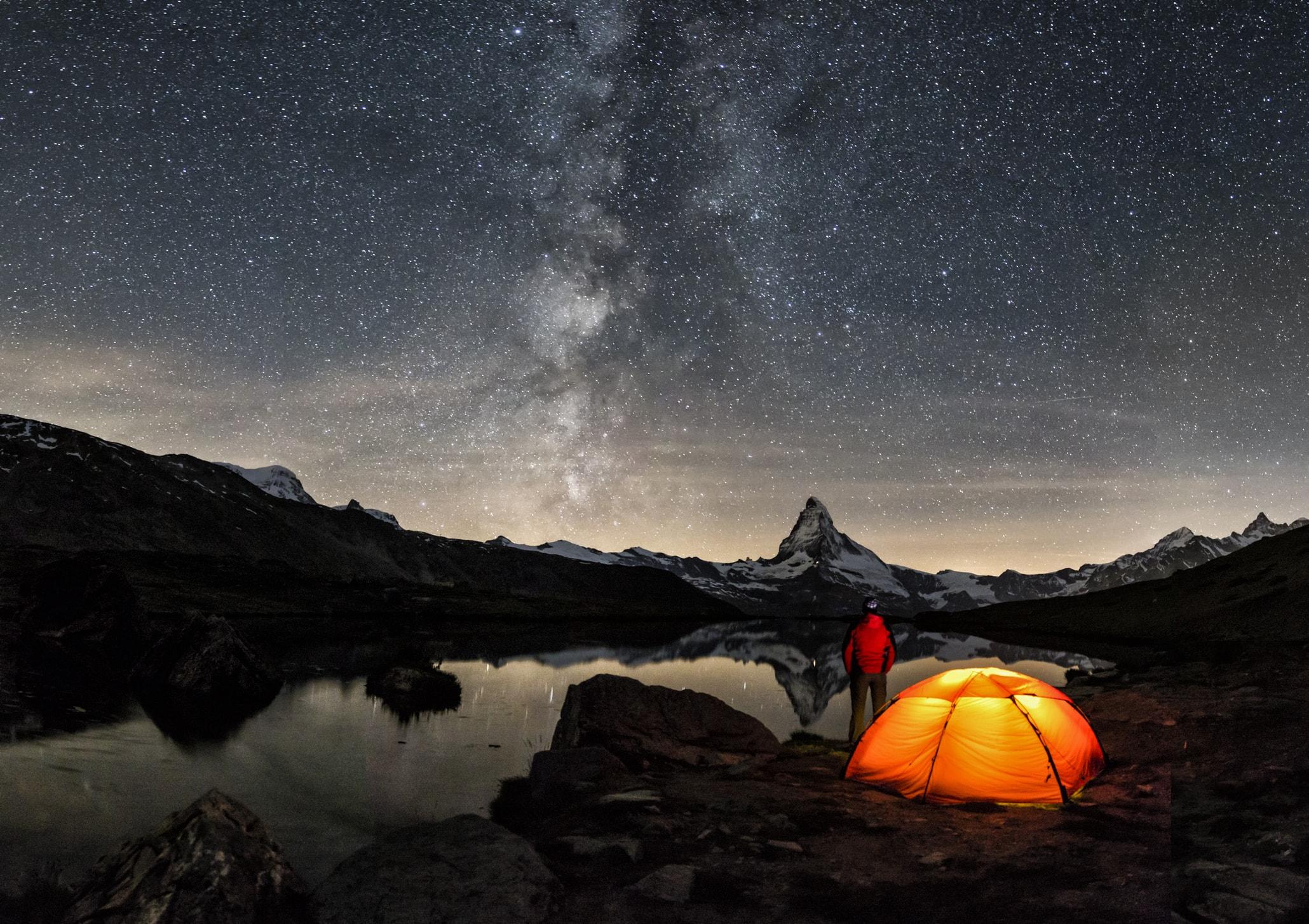 Eine Person zeltet in einer Berglandschaft mit n&auml;chtlichem Sternenhimmel