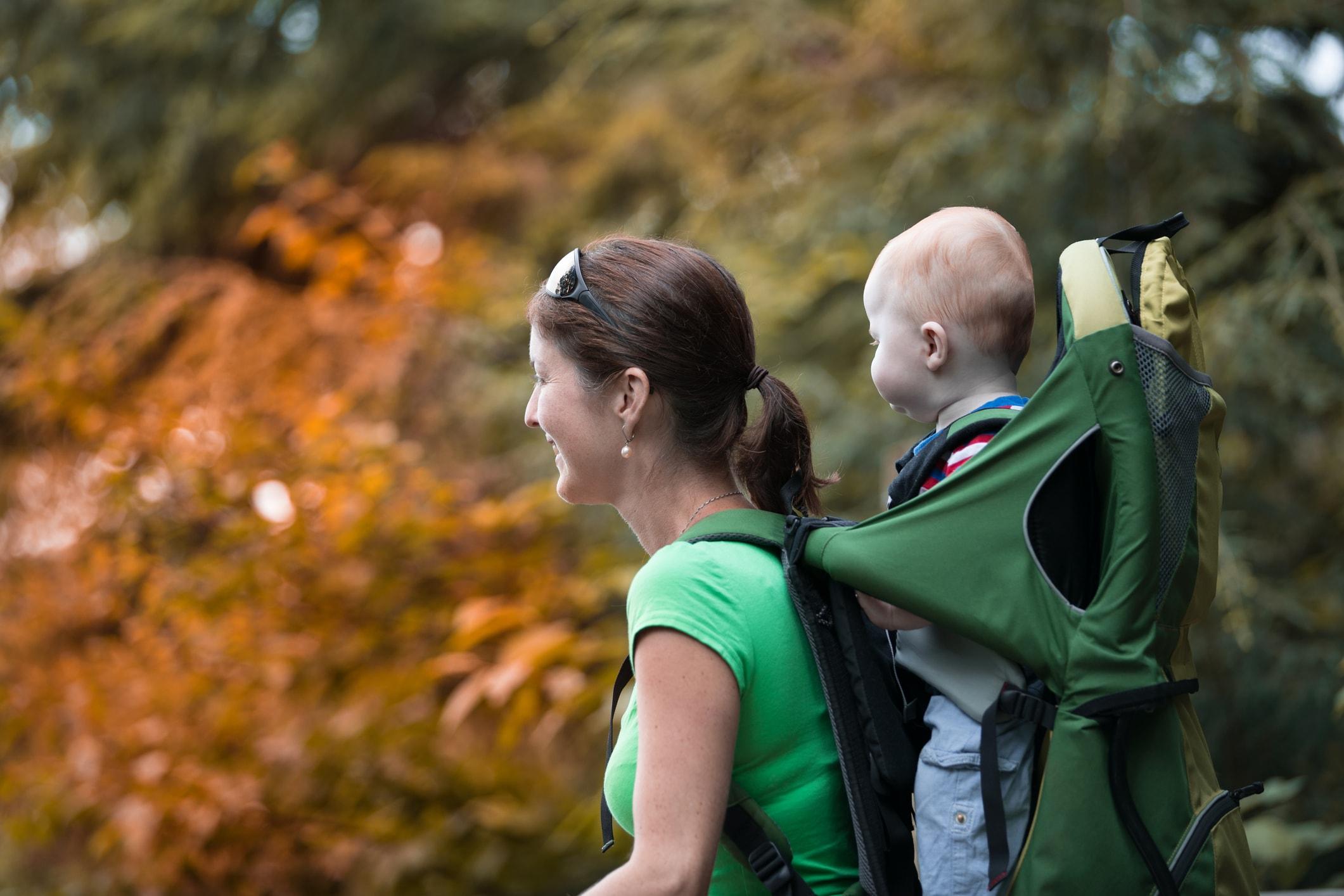 Eine Mutter trägt ihr kleines Kind auf dem Rücken in einer Kraxe.