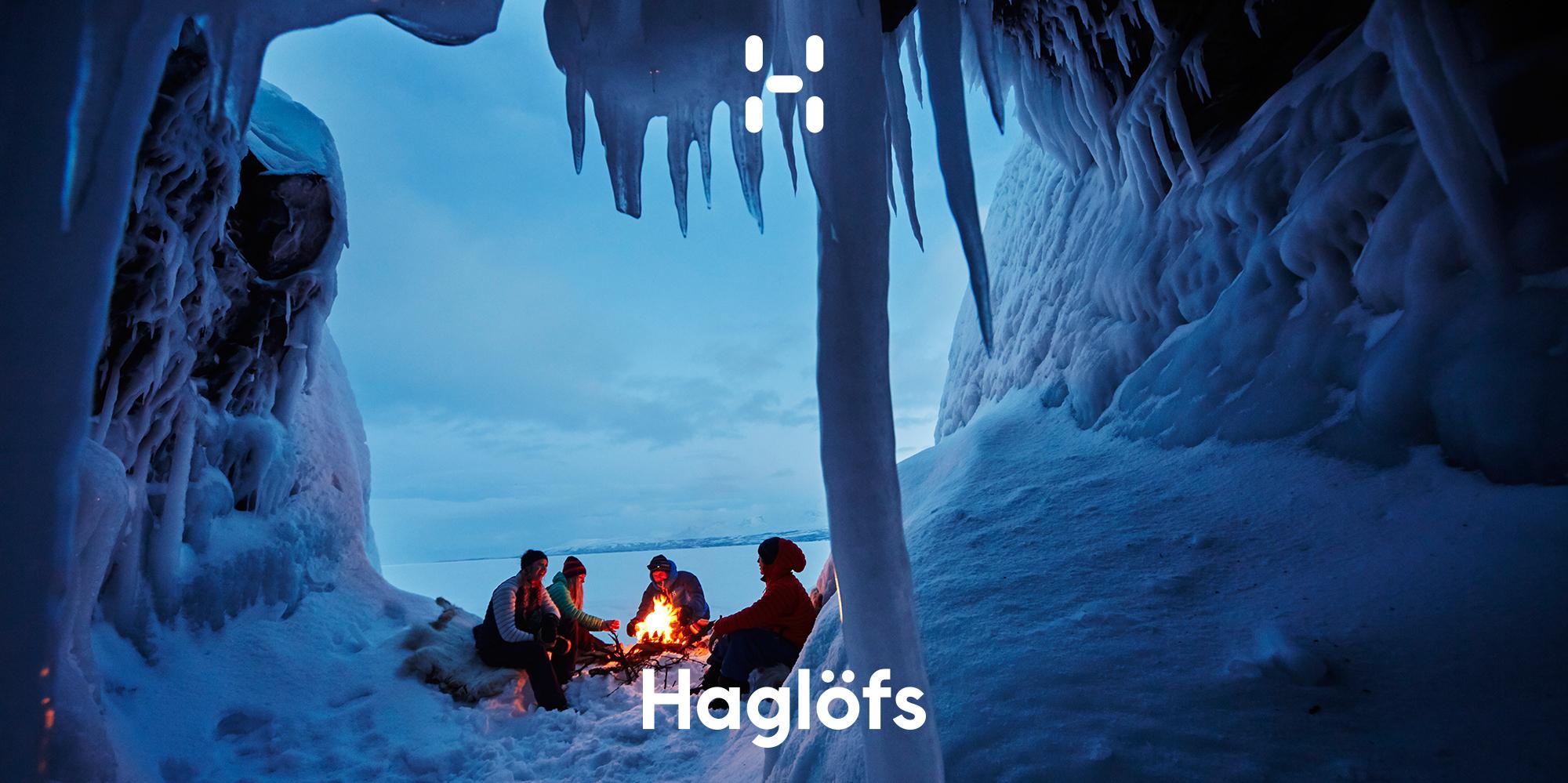 Eine Gruppe Skitourengeher sitzt um ein Feuer und w&auml;rmt sich bei einer Mahlzeit auf.