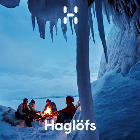 Eine Gruppe Skitourengeher sitzt um ein Feuer und wärmt sich bei einer Mahlzeit auf.