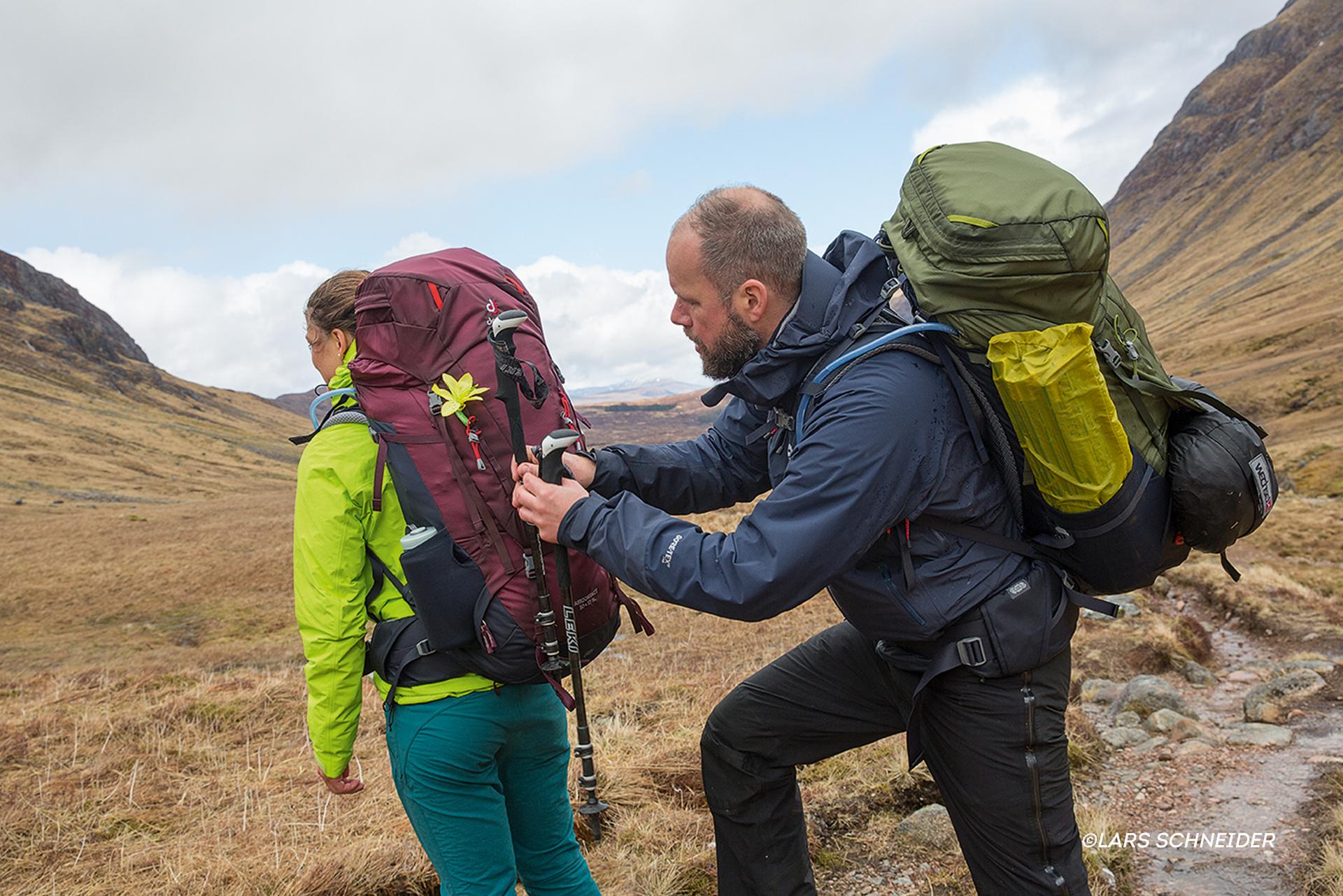 Ein Mann stellt die Schlaufen des Rucksacks einer Frau richtig ein.