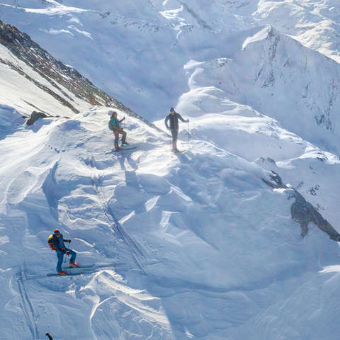 Eine Gruppe von drei Skitourengehern durchqueren eine schwierige Felsstelle.