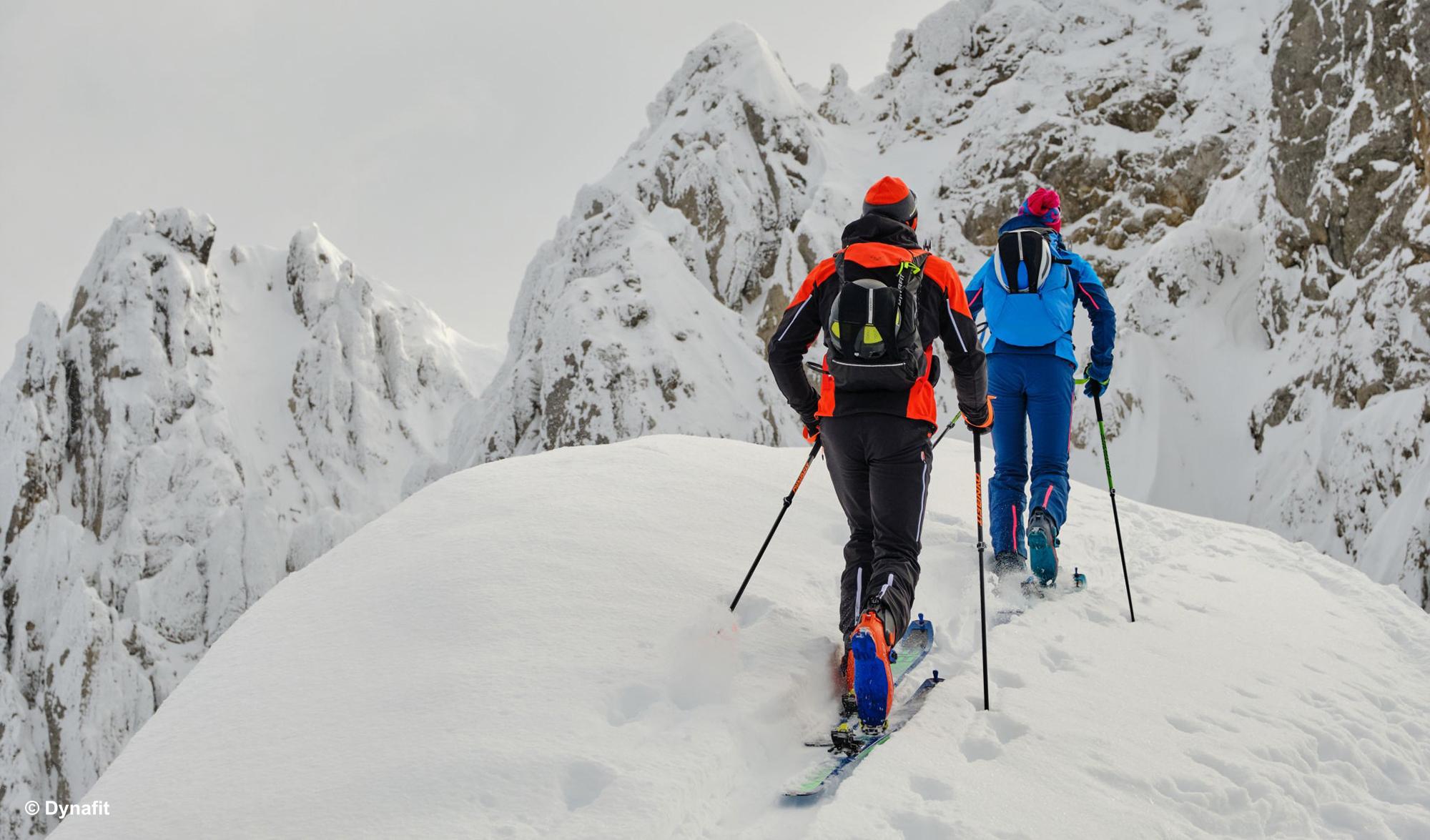 Zwei Skitourengeher auf Skihochtour gehen auf eine Felswand zu.