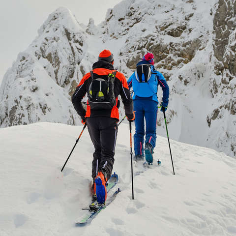 Zwei Skitourengeher auf Skihochtour gehen auf eine Felswand zu.