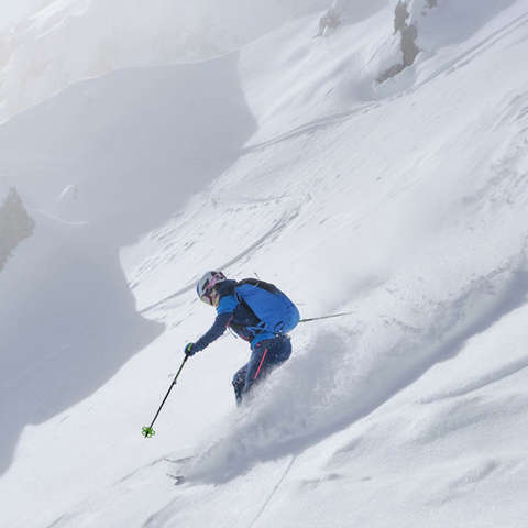 Ein Skitourengeher fährt einen Hang mit frischem Tiefschnee hinab.