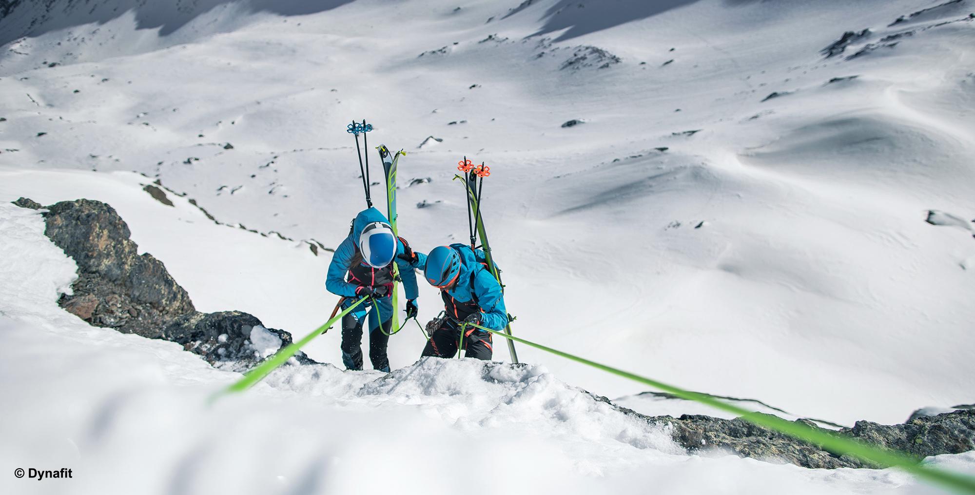 Zwei Skitourengeher auf Skihochtour seilen sich einen sehr steilen Felshang ab.