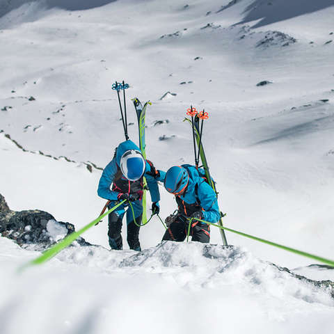 Zwei Skitourengeher auf Skihochtour seilen sich einen sehr steilen Felshang ab.