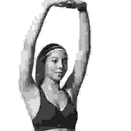 Eine Frau mit Stirnband hat die Arme über den Kopf gestreckt und trägt einen schwarzen Sport Bra von Nike.