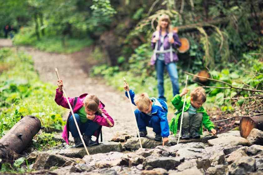 Drei Kinder spielen im Wald mit Stöcken