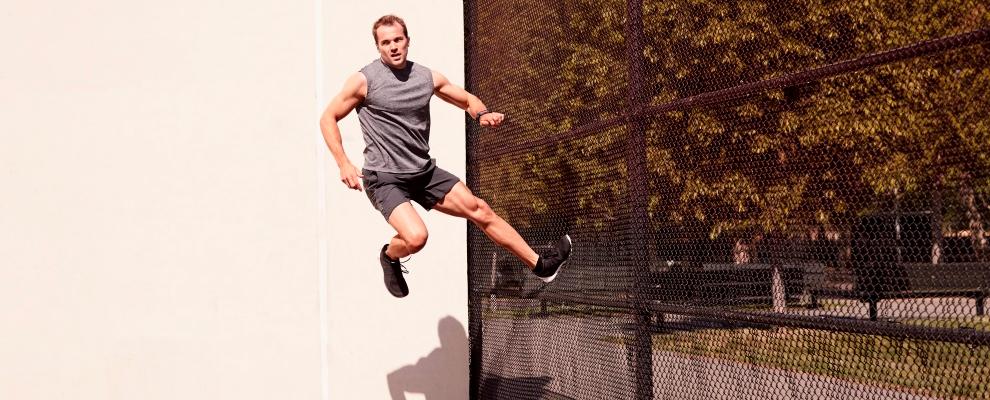 Ein Mann springt gegen einen schwarzen Zaun und scheint in der Luft zu schweben. 