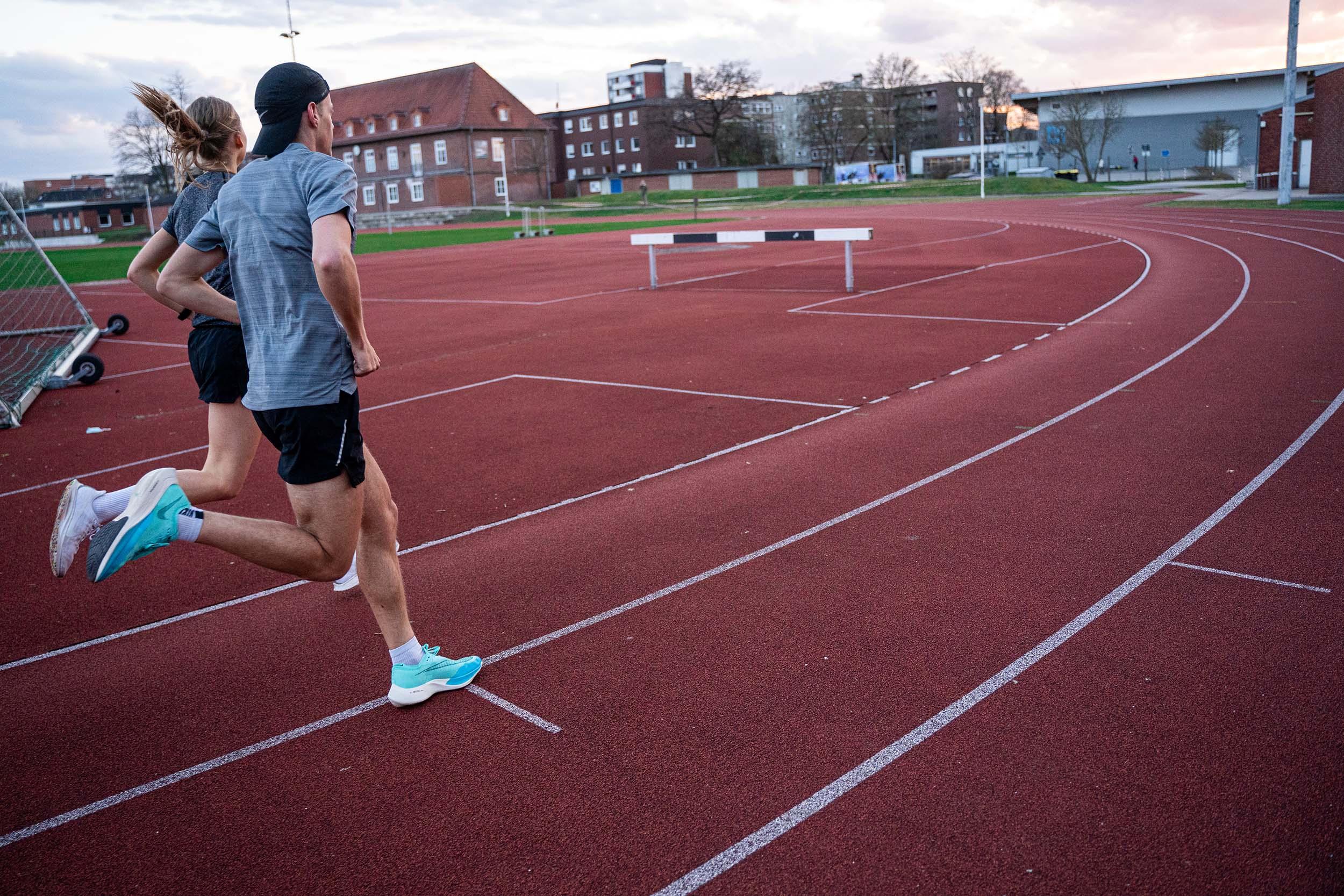 Eine Frau und ein Mann trainineren für einen Halbmarathon. Sie laufen auf einer Tartanbahn.