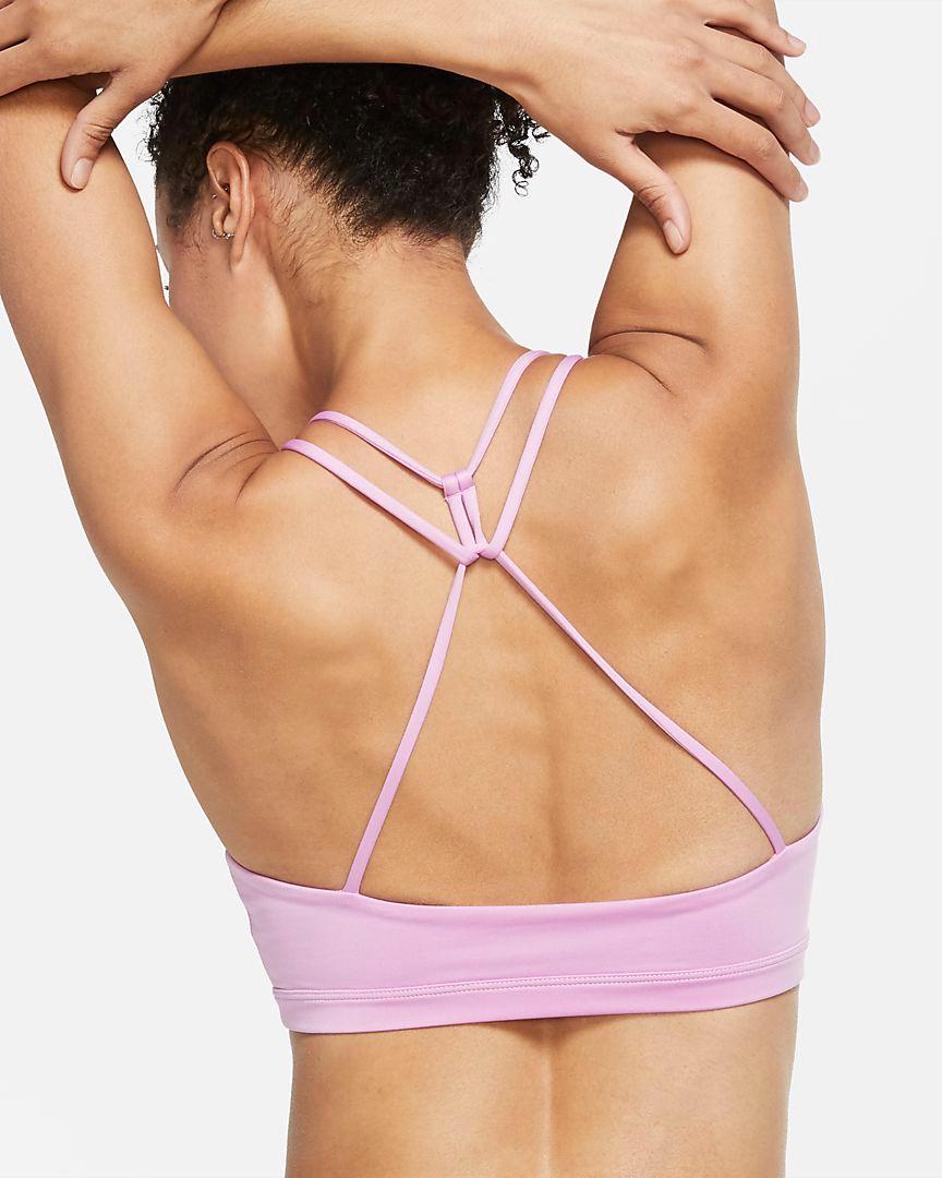 Eine Frau steht mit dem Rücken zur Kamera. Sie hat die Arme nach oben gestreckt und trägt einen rosa Nike Indy Sport-BH mit leichtem Halt.