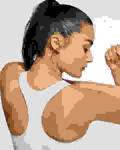 Eine Frau steht mit dem Rücken zur Kamera und dehnt ihre Arme. Sie trägt einen weißen Nike Swoosh Sport-BH mit mittlerem Halt.