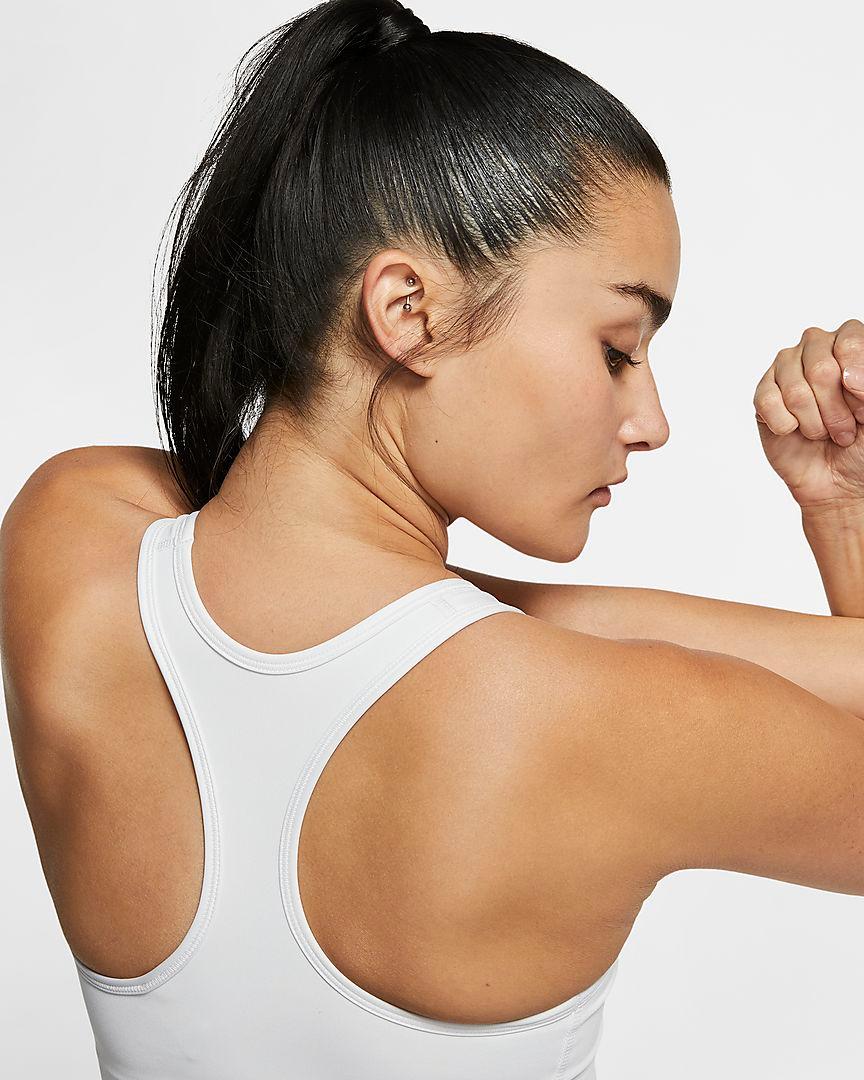 Eine Frau steht mit dem Rücken zur Kamera und dehnt ihre Arme. Sie trägt einen weißen Nike Swoosh Sport-BH mit mittlerem Halt.