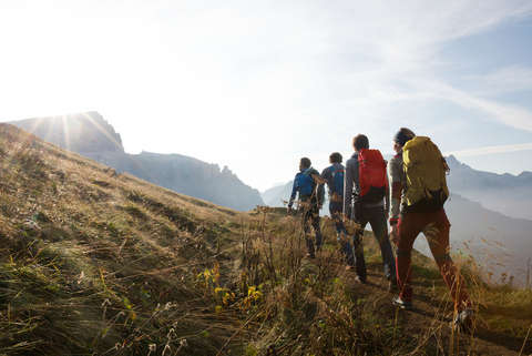 Ein Gruppe wandert mit Rucksäcken auf dem Rücken durch eine grüne Landschaft