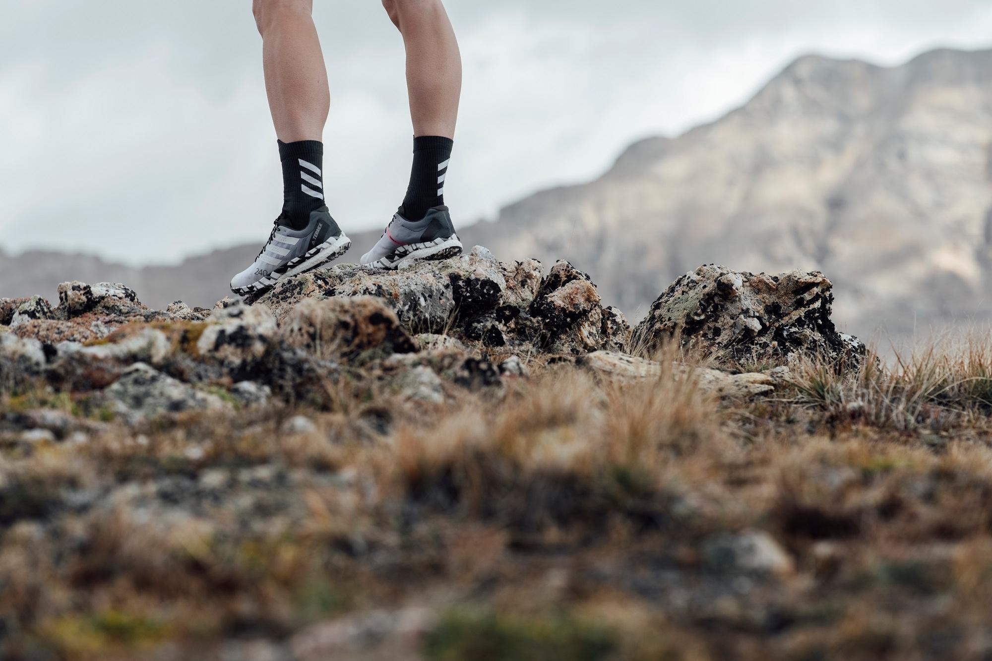 L&auml;ufer mit adidas Schuhen rennt &uuml;ber steiniges alpines Gel&auml;nde.