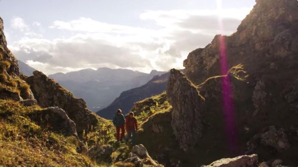 Zwei Personen wandern in einer sonnigen alpinen Landschaft