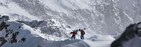 2 Bergsteiger haben ihre Skier geschultert und wandern durch eine verschneite Berglandschaft.