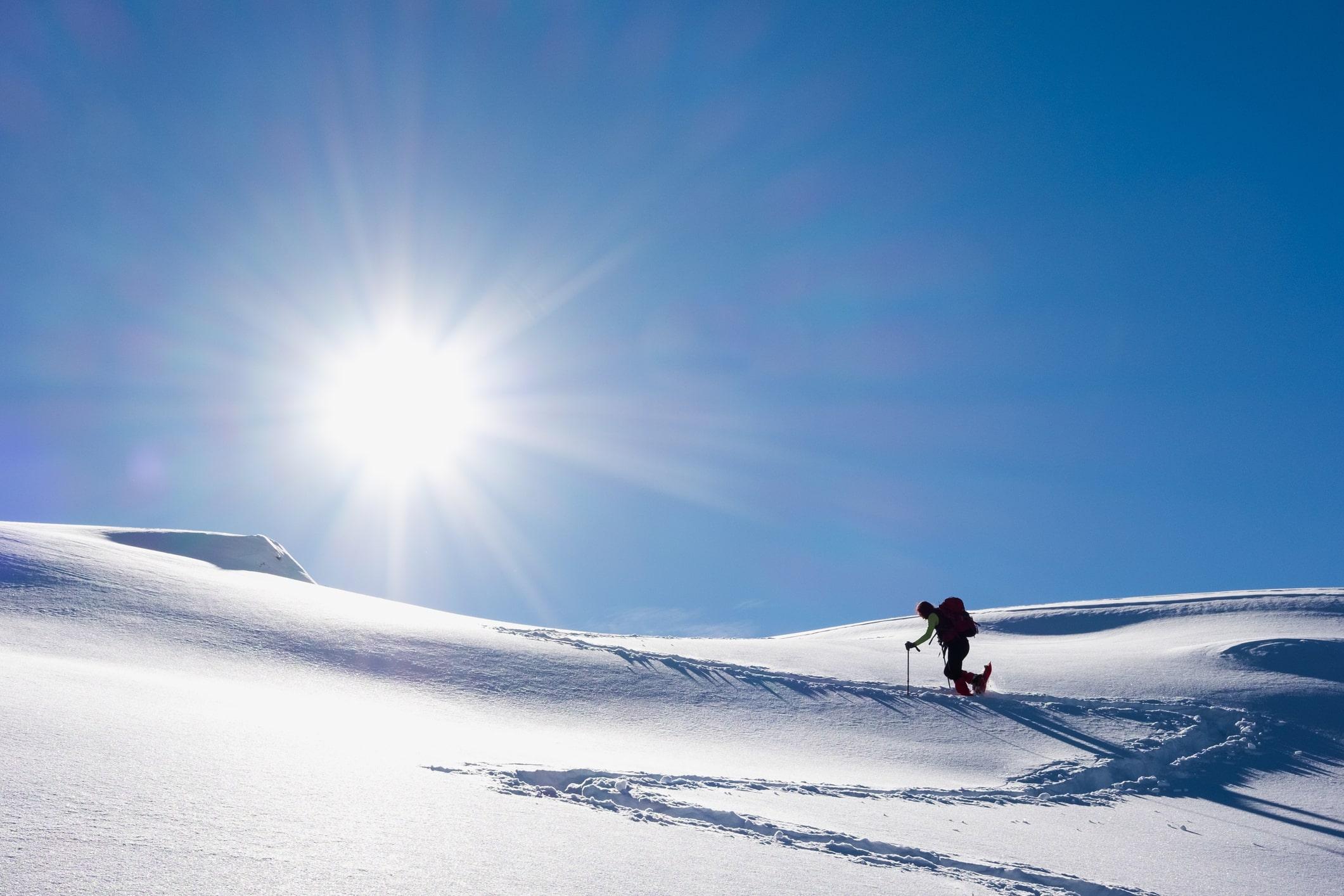 Ein Schneeschuhwanderer läuft in einer sonnigen Winterlandschaft