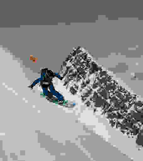 Ein Snowboarder fährt mit seinem Board einen steilen Abhang hinunter.