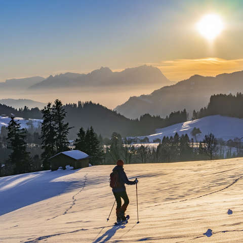Eine Frau wandert mit Schneeschuhen durch eine Schneelandschaft bei Sonnenuntergang