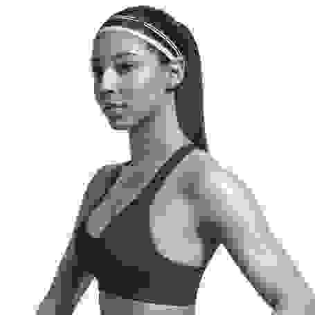 Eine Frau steht seitlich zur Kamera und trägt einen schwarzen Sport BH von Nike.