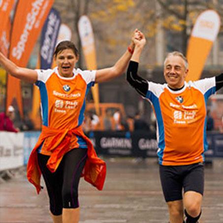 Eine Frau und ein Mann jubeln laufend bei einem Sportscheck-Stadtlauf