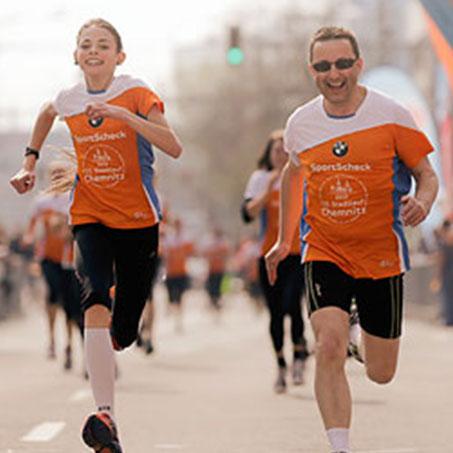 Ein Mann und eine Frau laufen lachend um die Wette beim Stadtlauf Chemnitz.