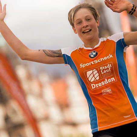 Eine Läuferin reißt freudig die Arme noch oben nachdem sie den Stadtlauf Dresden erfolgreich gemeistert hat.