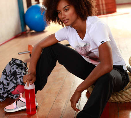 Eine Frau sitzt mit einer Trinkflasche auf dem Boden eines Fitnessstudios.
