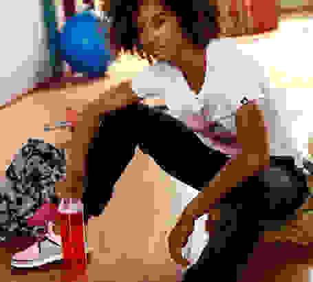 Eine Frau sitzt mit einer Trinkflasche auf dem Boden eines Fitnessstudios.