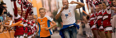 Ein junger Teilnehmer läuft die Zielgerade beim SportScheck Stadtlauf Magedeburg entlang. Hinter ihm läuft ein Moderator mit Mikrofon in der Hand.