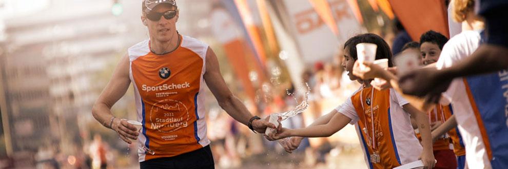 Ein Läufer beim Nürnberg Stadtlauf nimmt Becher mit Wasser während des Laufens entgegen.