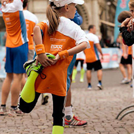 Ein junges Mädchen beim Dehnen der Oberschenkelmuskulatur kurz vor Beginn des Braunschweiger Stadtlaufs.