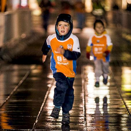 EIn kleiner Junge läuft bei einem Stadtlauf bei Regen durch die Straßen