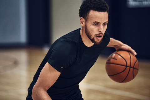Steph Curry trainiert Basketball in einer Basketball-Halle und trägt dabei ein Shirt der Under Armour Curry Kollektion.