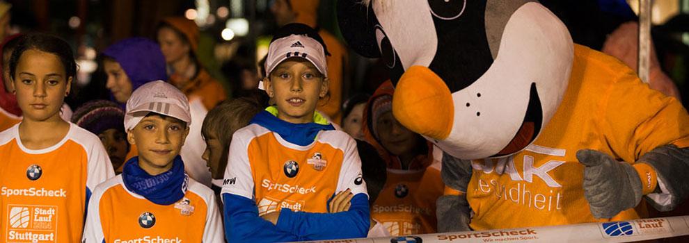 Drei Kinder und ein Maskottchen in Sportscheck-Shirts bei einem Stadtlauf