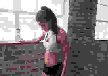 Eine Frau ruht sich während des Trainings aus. Sie steht an einer Steinwand mit einer Wasserflasche in der Hand.
