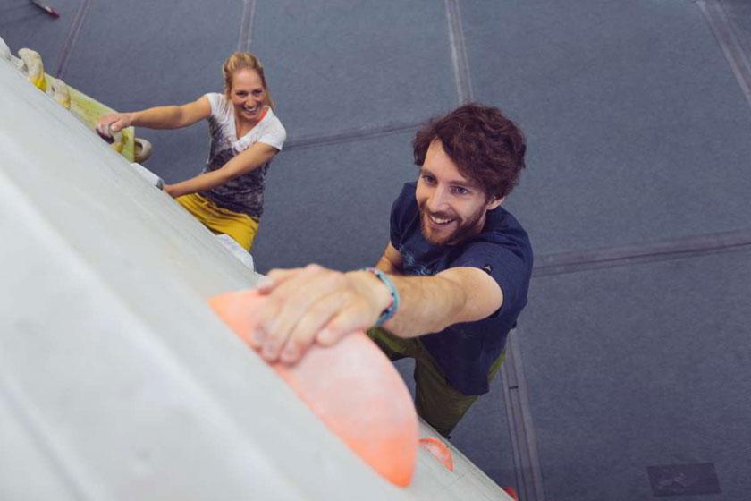 Ein Mann und eine Frau bouldern an einer Kunstwand in einer Boulderhalle. Sie sind von oben fotografiert.