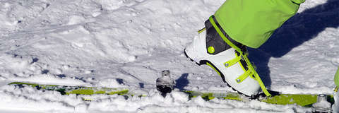 Ein Tourenskischuh und die Bindung an einem Tourenski im Schnee in der Nahaufnahme.