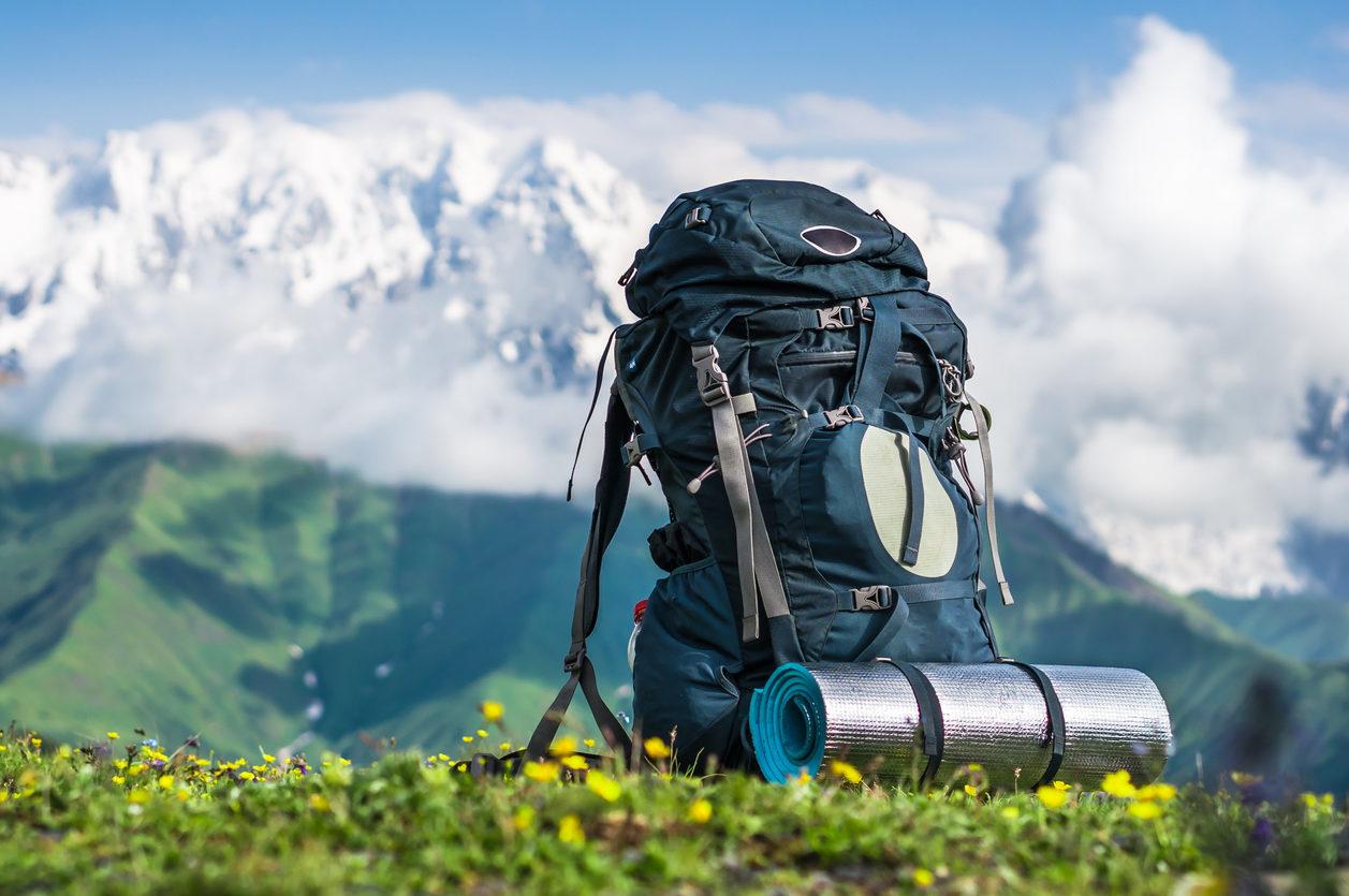 Ein Rucksack steht auf einer Wiese. Im Hintergrund ist ein Bergpanorama zu sehen.