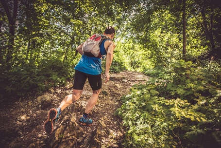 Ein Mann beim Trail Running in einem Wald. Auf dem Rücken trägt er einen Trailrunning Rucksack.