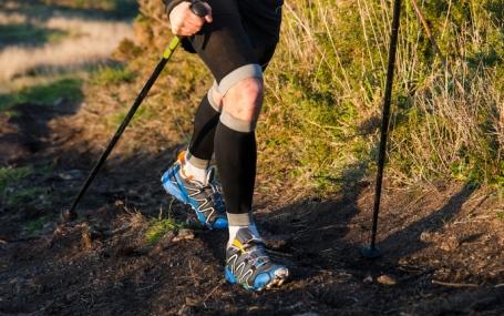 Nahaufnahme der Beine eines Läufers mit Walkingstöcken in der Natur
