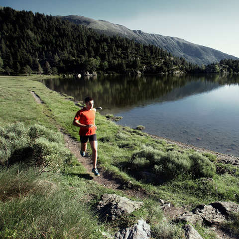 Ein Trailrunner läuft an einem Bergsee entlang.