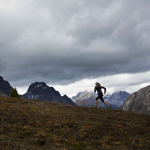 Eine Trailrunnerin läuft ber regnerischem Wetter über eine Bergwiese.