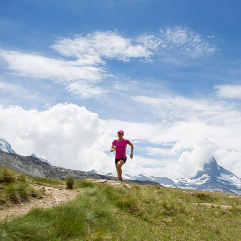 Eine Trailrunnerin läuft einen Trail während das Matterhorn im Hintergrund ist.