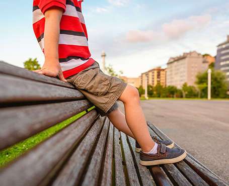 Ein Junge sitzt auf der Lehne einer Parkbank mit seinen Kinderschuhen auf der Sitzfläche.